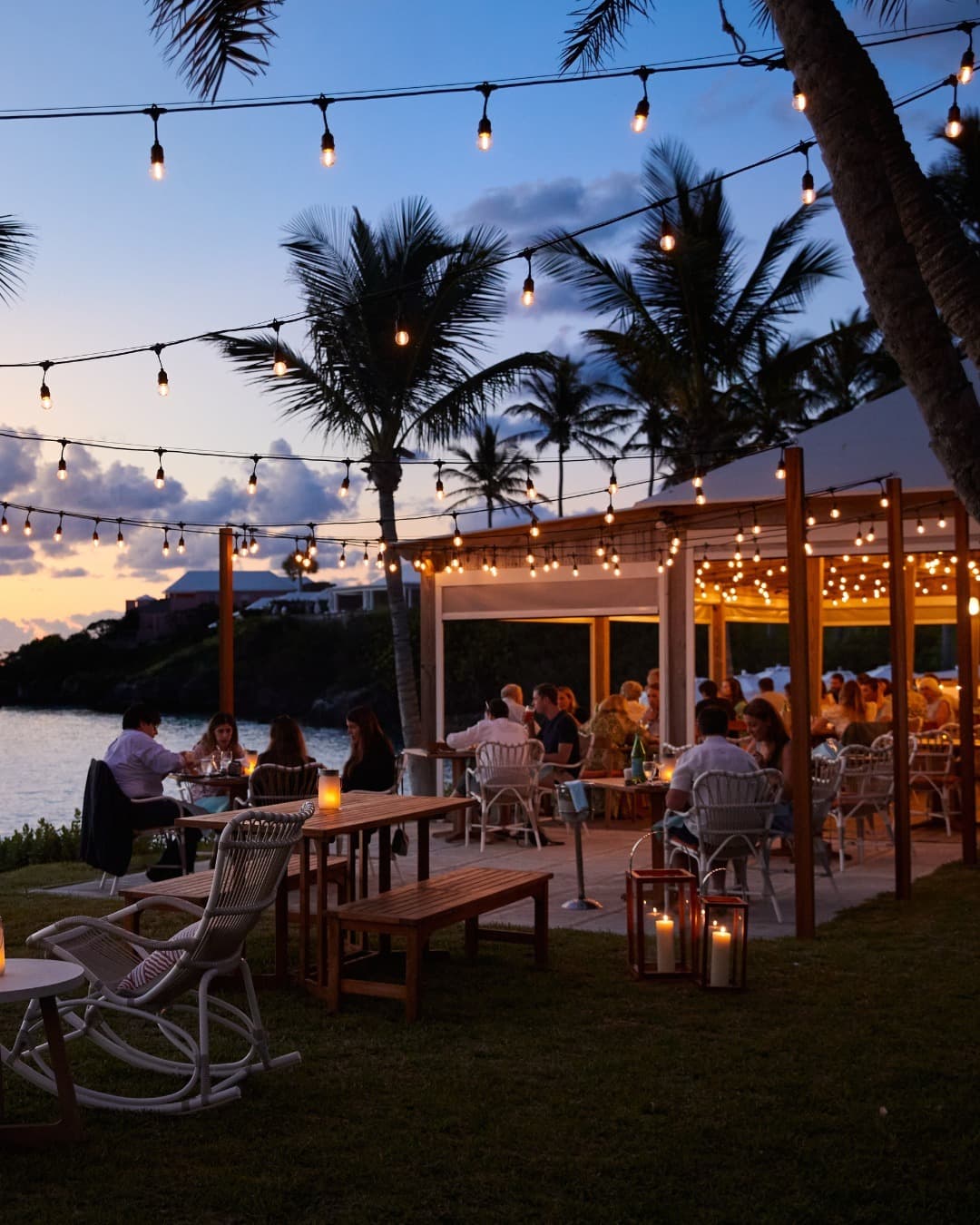 A waterside Bermuda terrace lit by string lights at dusk